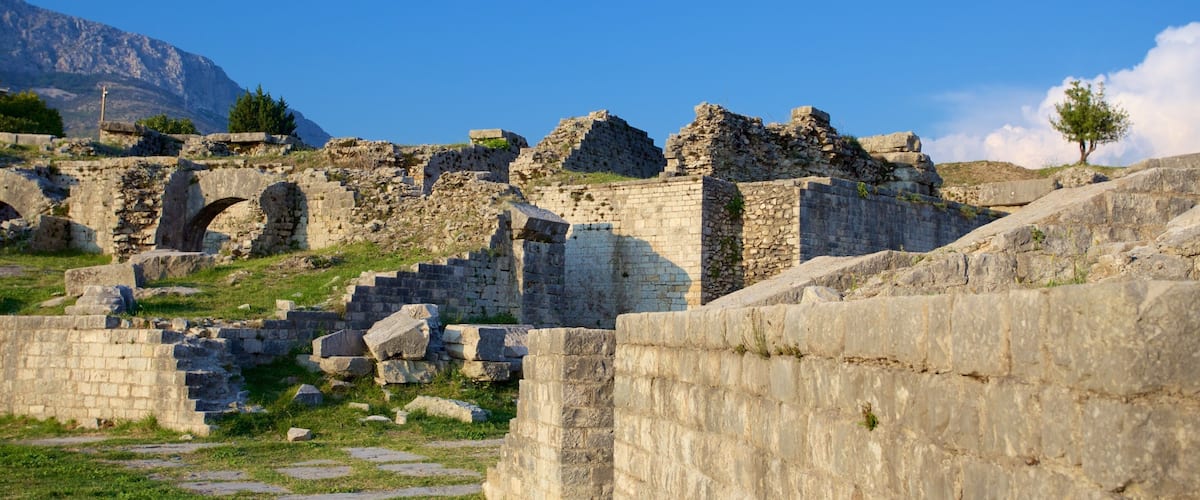 Ancient ruins with stone walls and arches, set against a mountainous backdrop.