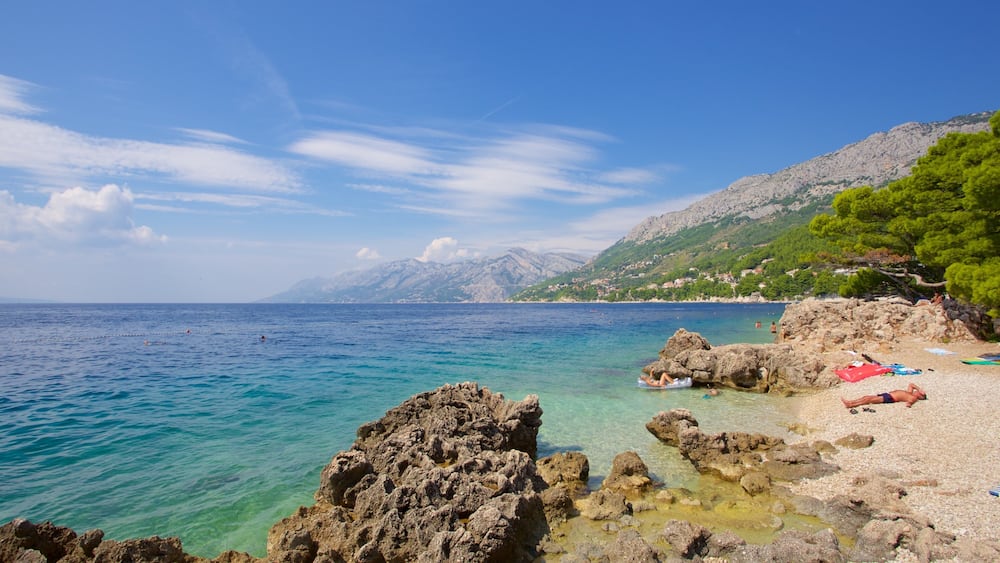 Eine Küstenlandschaft mit klarem türkisblauem Wasser, felsigen Ufern und einem Bergpanorama im Hintergrund.