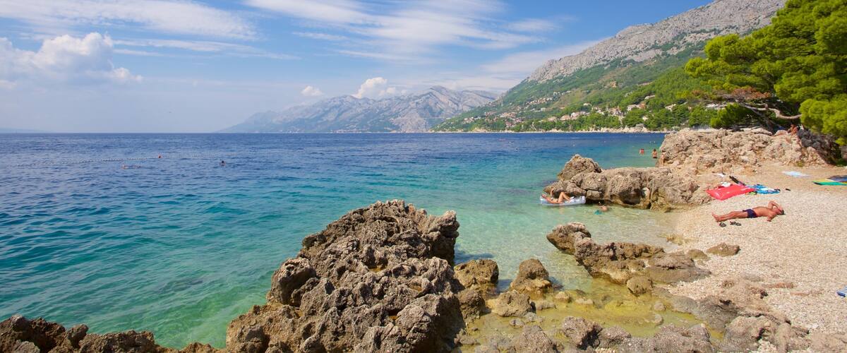 A coastal landscape with clear turquoise waters, rocky shorelines, and a backdrop of mountains.