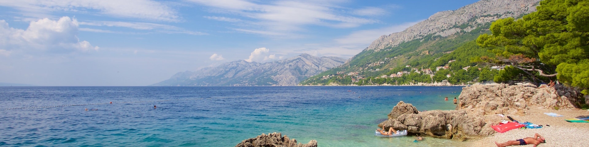 A coastal landscape with clear turquoise waters, rocky shorelines, and a backdrop of mountains.