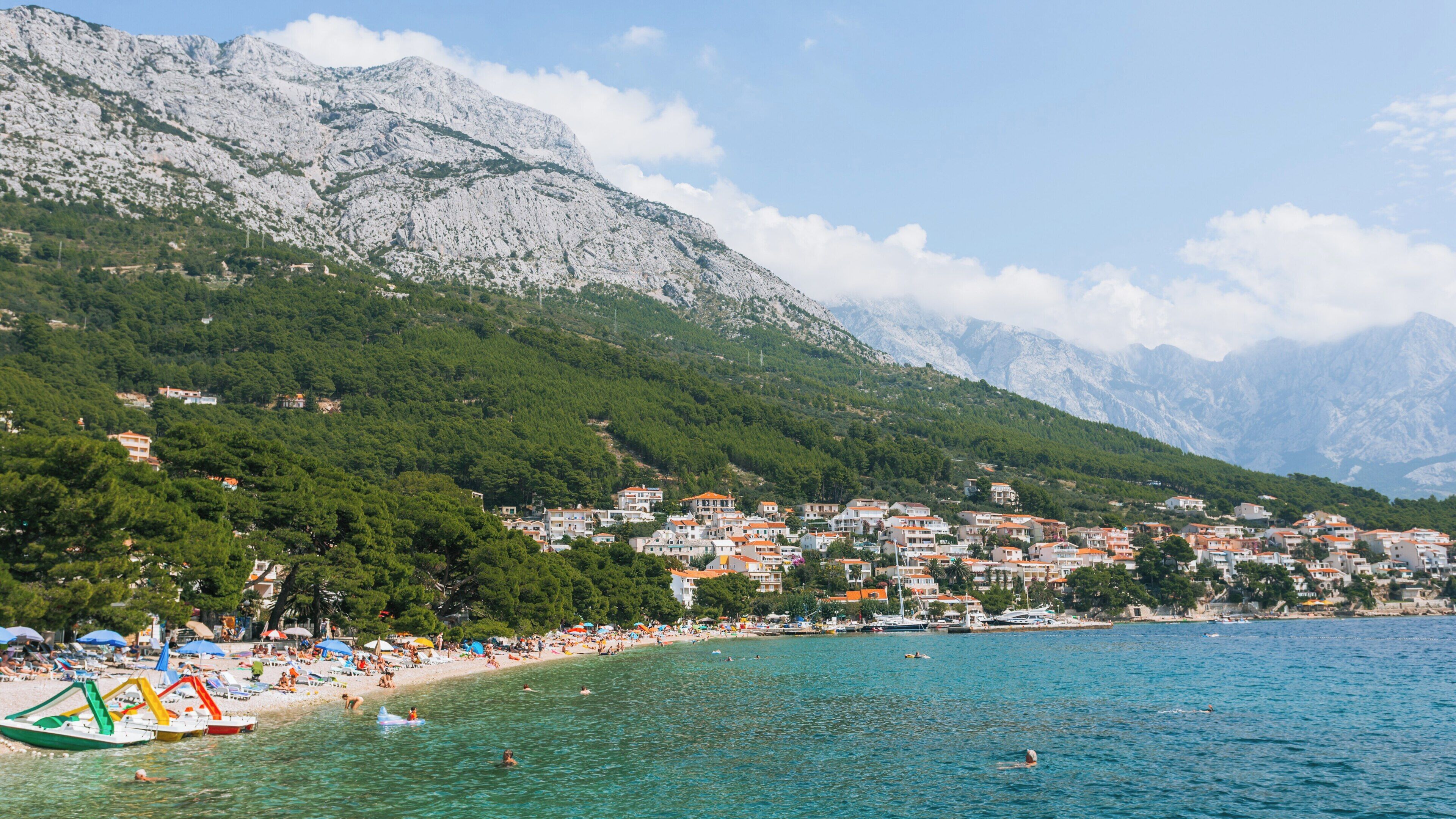 Beautiful Brela Beach in Split-Dalmatia, Croatia, invites visitors to relax and enjoy a sunny day by the crystal-clear Adriatic Sea with mountainous backdrop