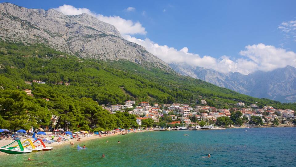 A coastal town with a beach, boats, and mountains in the background.