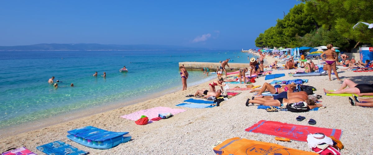 A crowded beach with people sunbathing, swimming, and playing in the water.