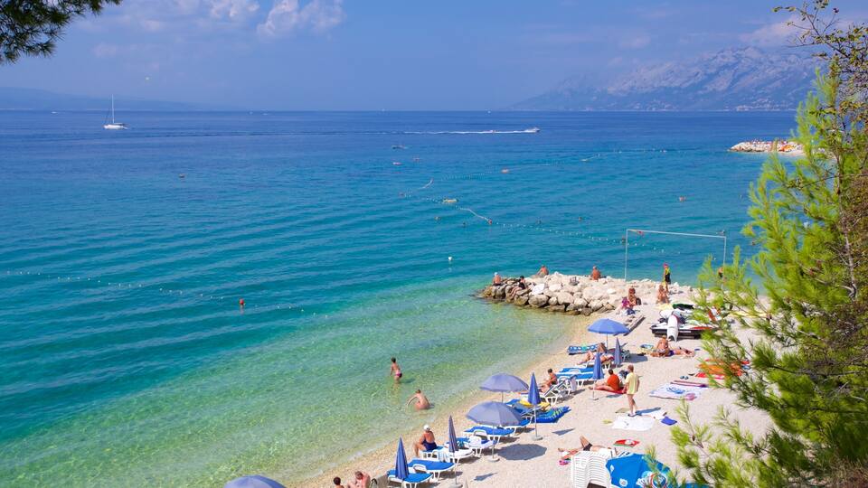 A beach with clear turquoise water, people sunbathing, and a sailboat in the distance.