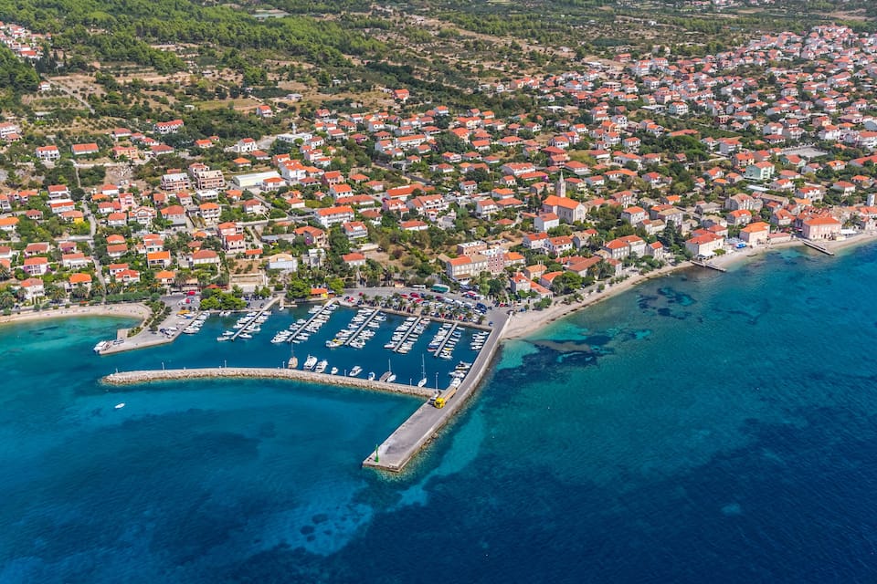 An aerial view of a coastal town with a marina, dense housing, and a beach.