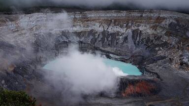 A geothermal area with a turquoise pool surrounded by steam and rocky terrain.