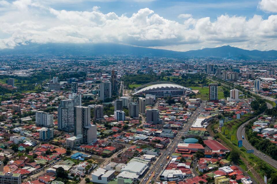 A cityscape with a prominent stadium, high-rise buildings, and a mountainous backdrop.
