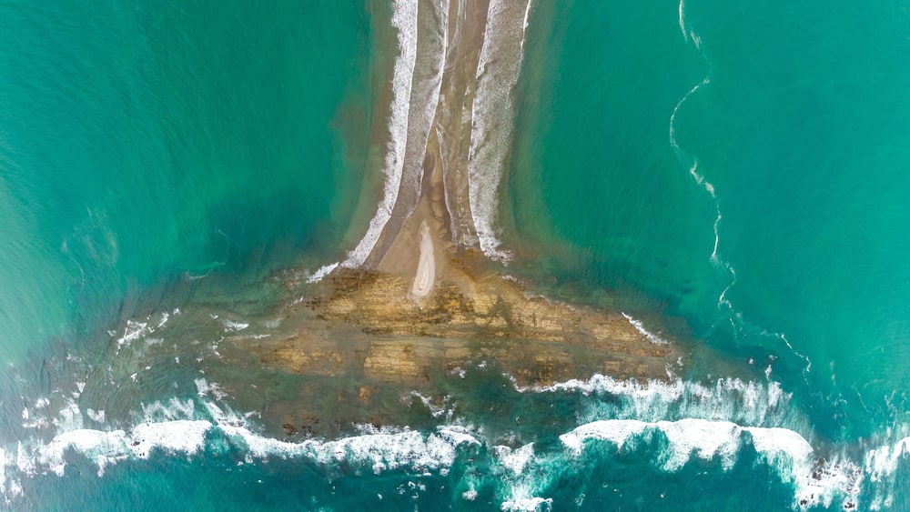 A coastal landscape with a sandy beach, a narrow waterway, and a large body of turquoise water.