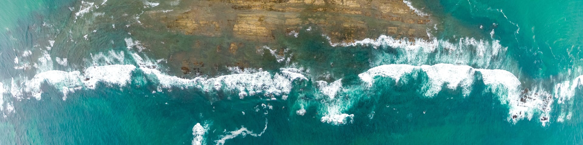A coastal landscape with a sandy beach, a narrow waterway, and a large body of turquoise water.