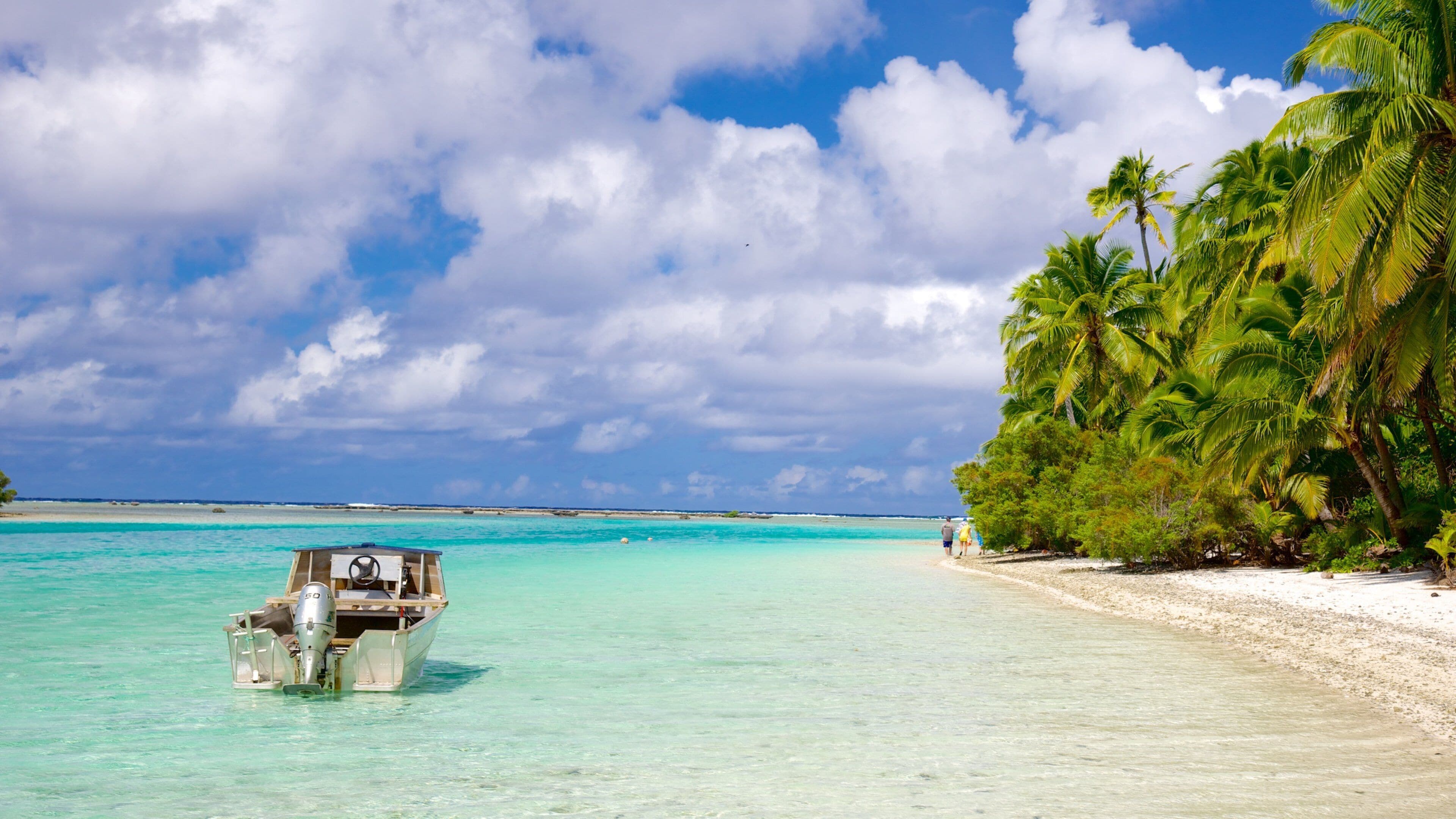 A boat on turquoise water, a sandy beach, and palm trees.