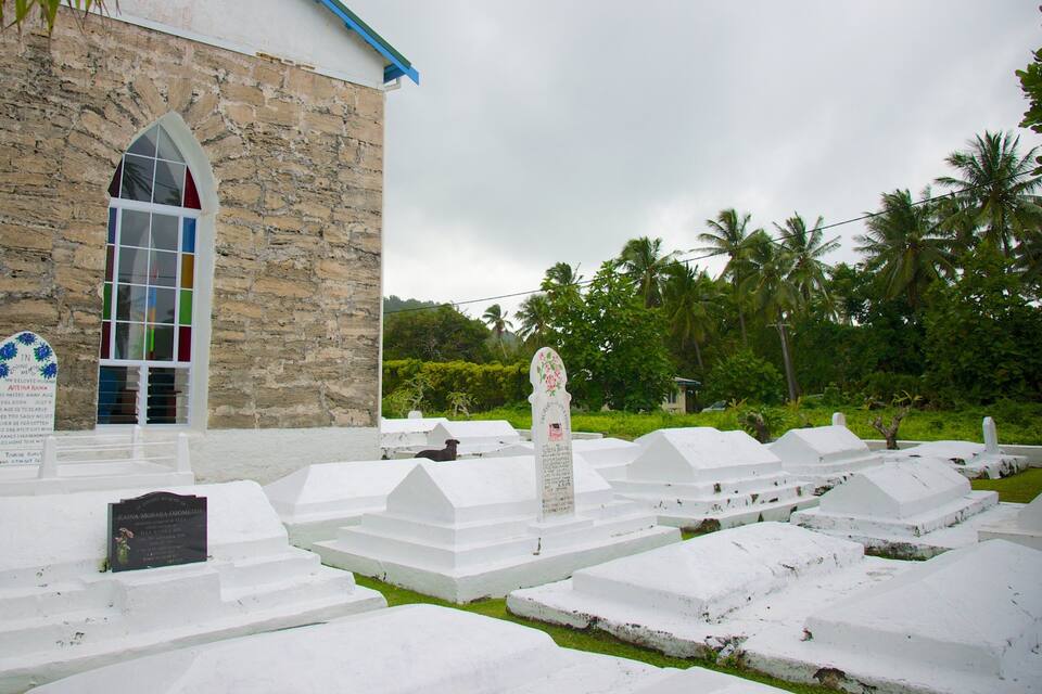 Un edificio de piedra con ventanas de arco, una cruz blanca y un cementerio con lápidas blancas.