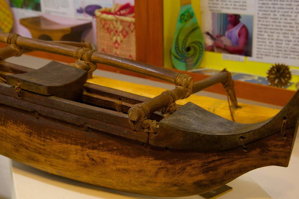 Un bote de madera con proa puntiaguda y popa plana, con un mástil central y dos remos laterales.