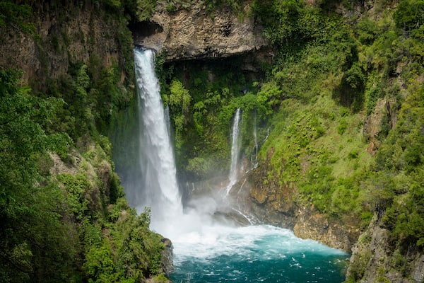 A waterfall cascading into a turquoise pool surrounded by lush greenery.