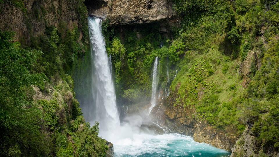 A waterfall cascading into a turquoise pool surrounded by lush greenery.