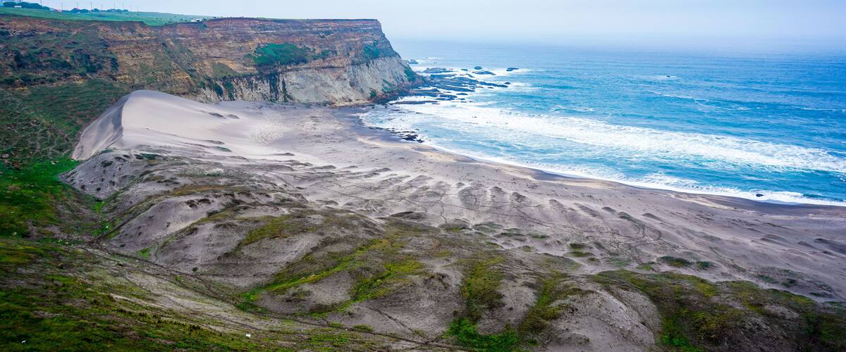 A coastal landscape with a sandy beach, cliffs, and ocean waves.