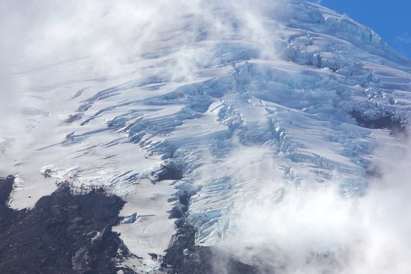 A snow-covered mountain with visible ice formations and a clear blue sky.