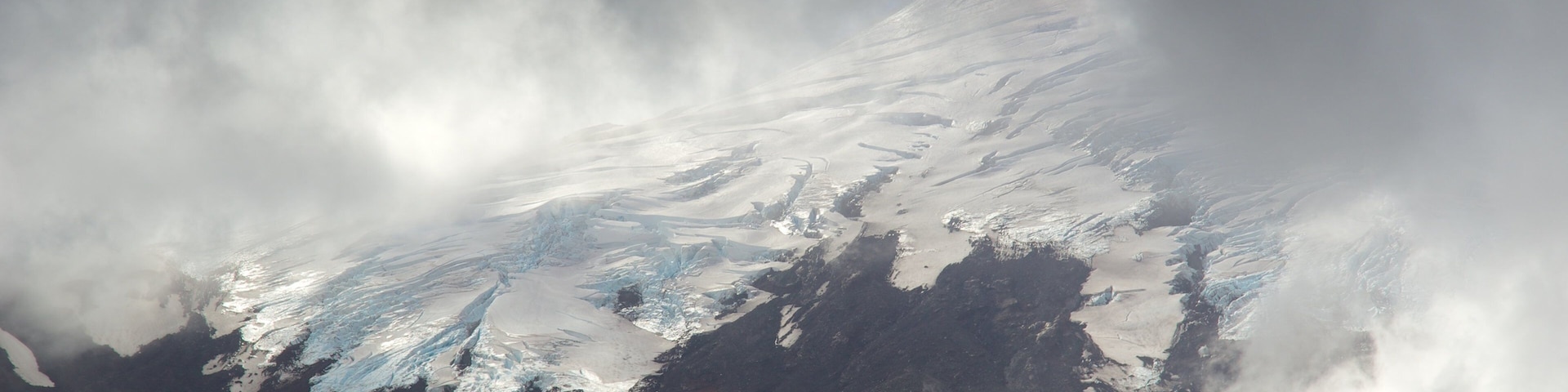 Montanha coberta de neve, parcialmente escondida por nuvens.