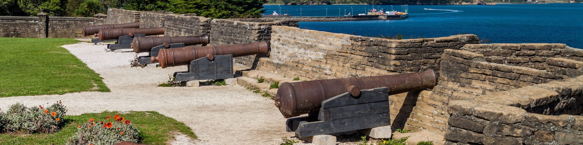 A coastal fort with cannons, a grassy area, and a ship in the background.