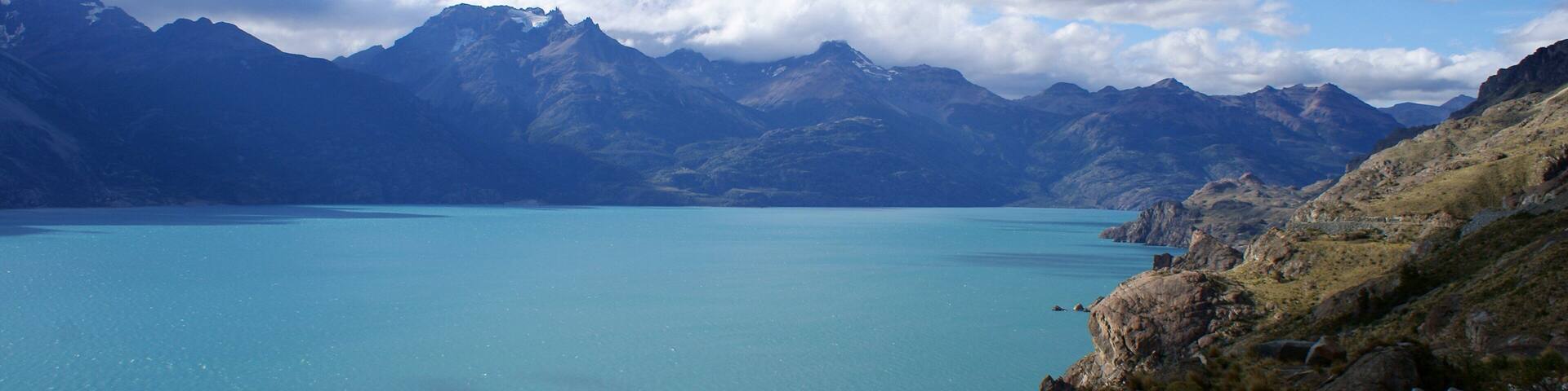 A mountain lake with clear blue water surrounded by rugged mountains and rocky terrain.