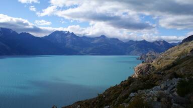 A mountain lake with clear blue water surrounded by rugged mountains and rocky terrain.