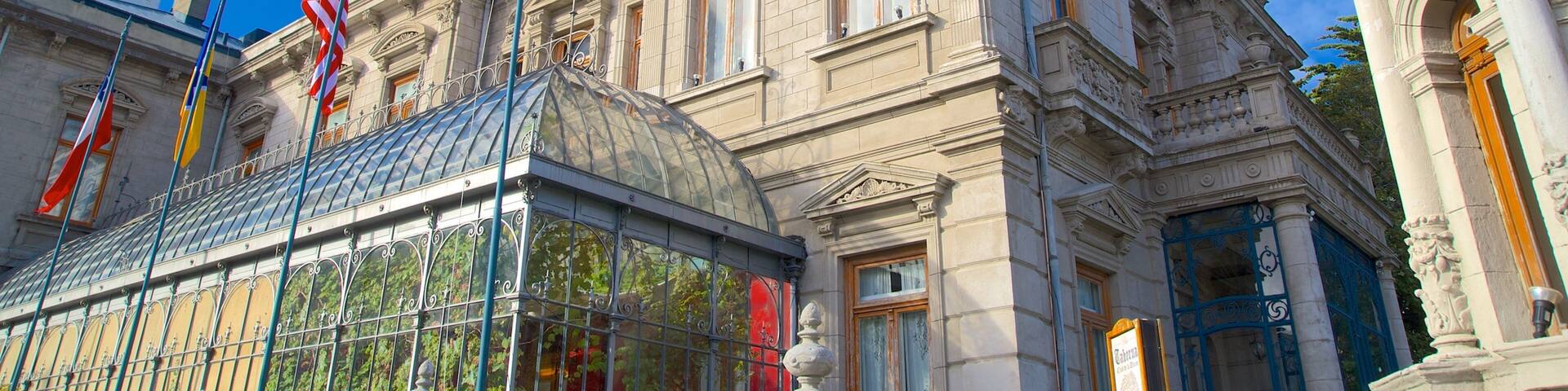 A historic building with ornate architecture, a glass conservatory, and multiple flags.