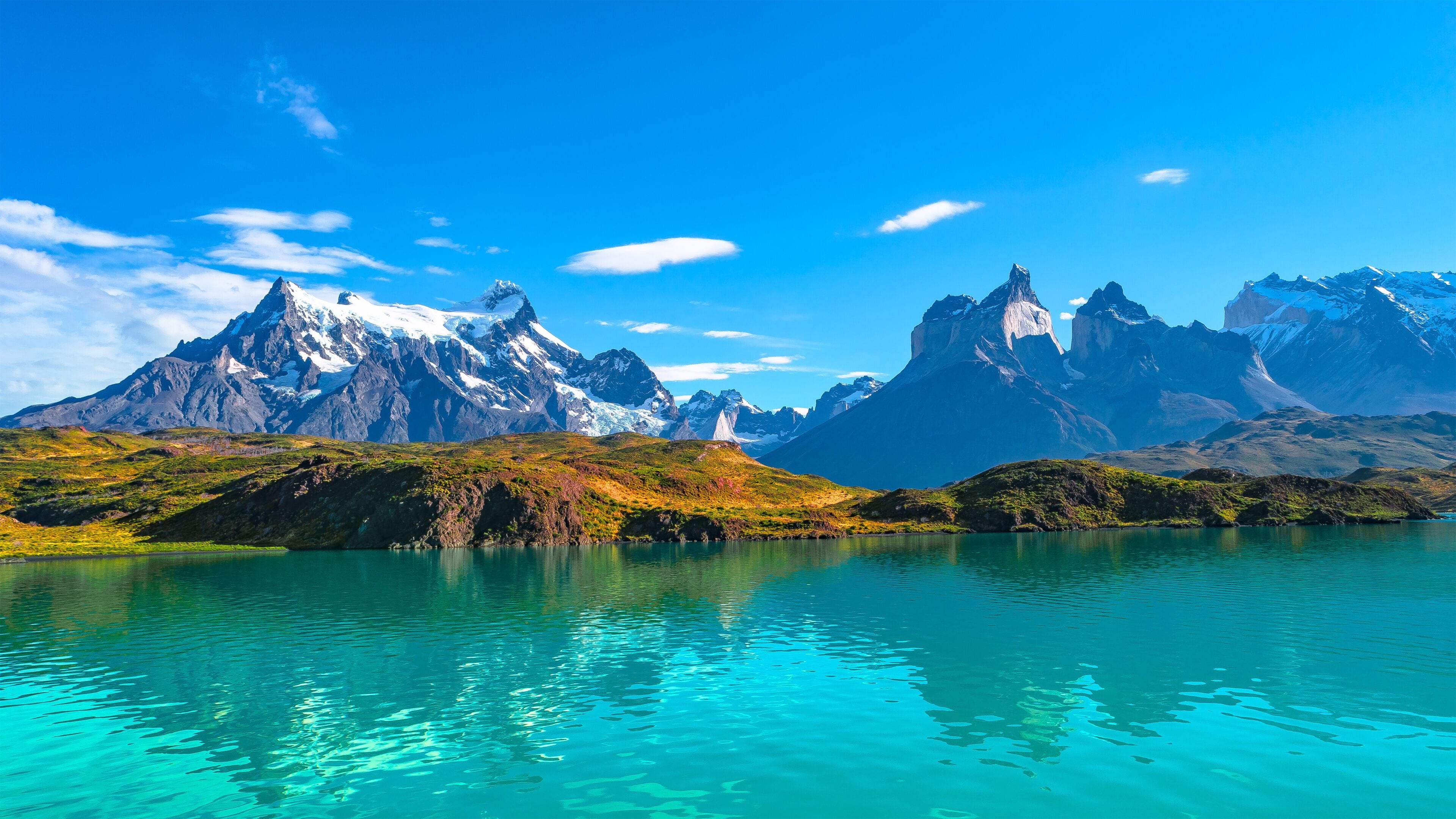 Cordillera con picos nevados y un lago turquesa que refleja el cielo.