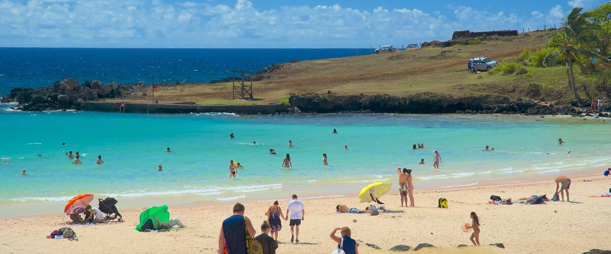 A beach with clear turquoise water, people swimming and sunbathing, and a rocky shoreline.