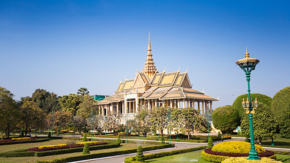 A traditional building with a tiered roof and a spire, surrounded by well-manicured gardens and a clear blue sky.