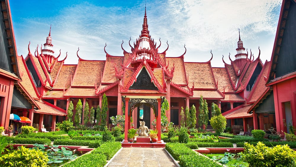 Et traditionelt thai tempel med en central statue, omgivet af frodigt grønt og en klar blå himmel.
