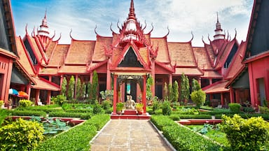 A traditional Thai temple with a central statue, surrounded by lush greenery and a clear blue sky.
