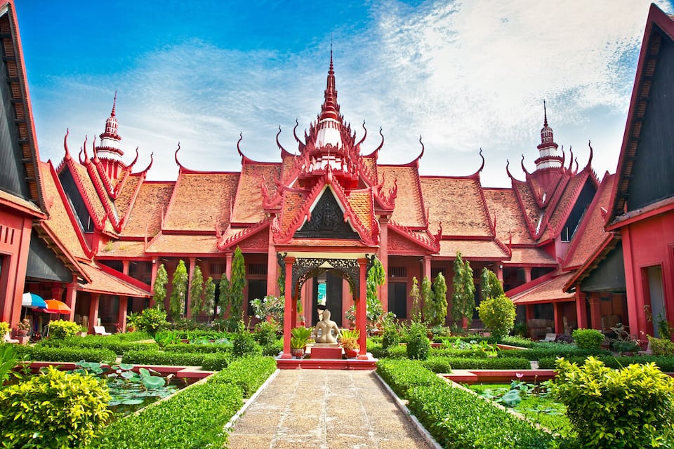 A traditional Thai temple with a central statue, surrounded by lush greenery and a clear blue sky.