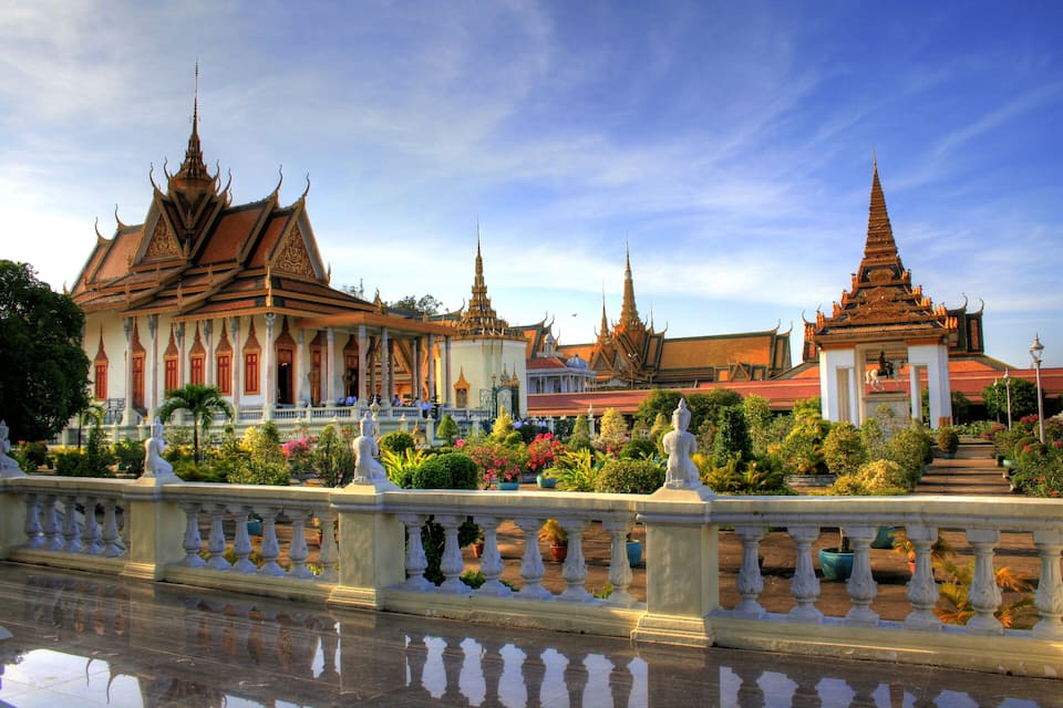 A traditional Thai temple with ornate architecture, a reflective waterway, and a well-maintained garden.