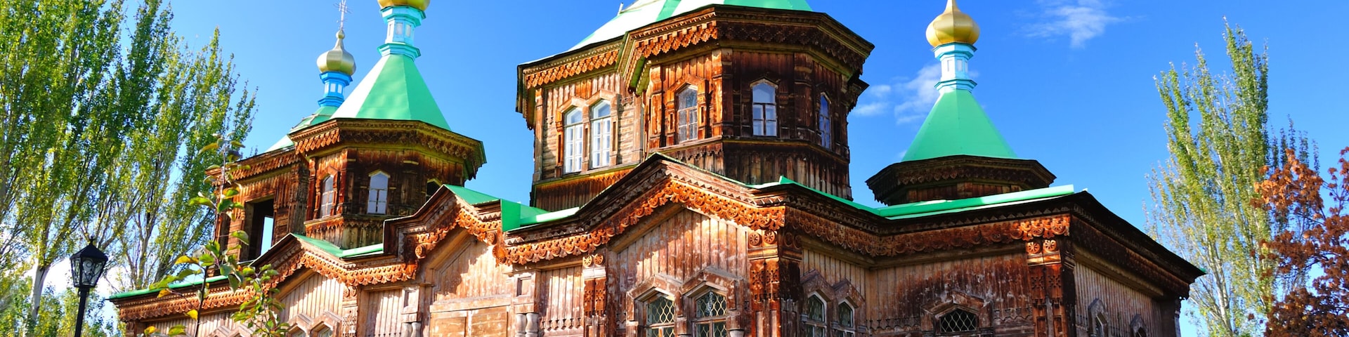 A wooden church with green domes and a cross on top, surrounded by trees.