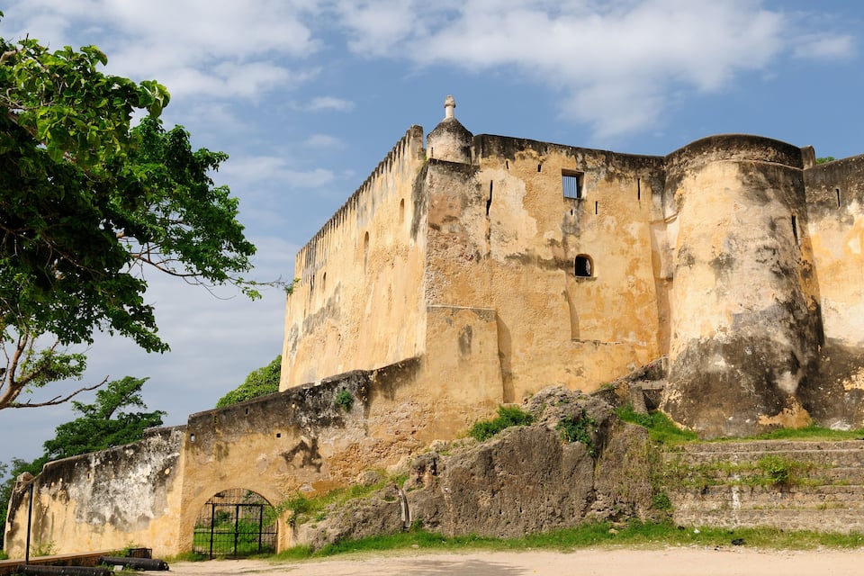 Un vieux fort doté d’une grande porte, entouré de verdure et surplombé d’un ciel dégagé.