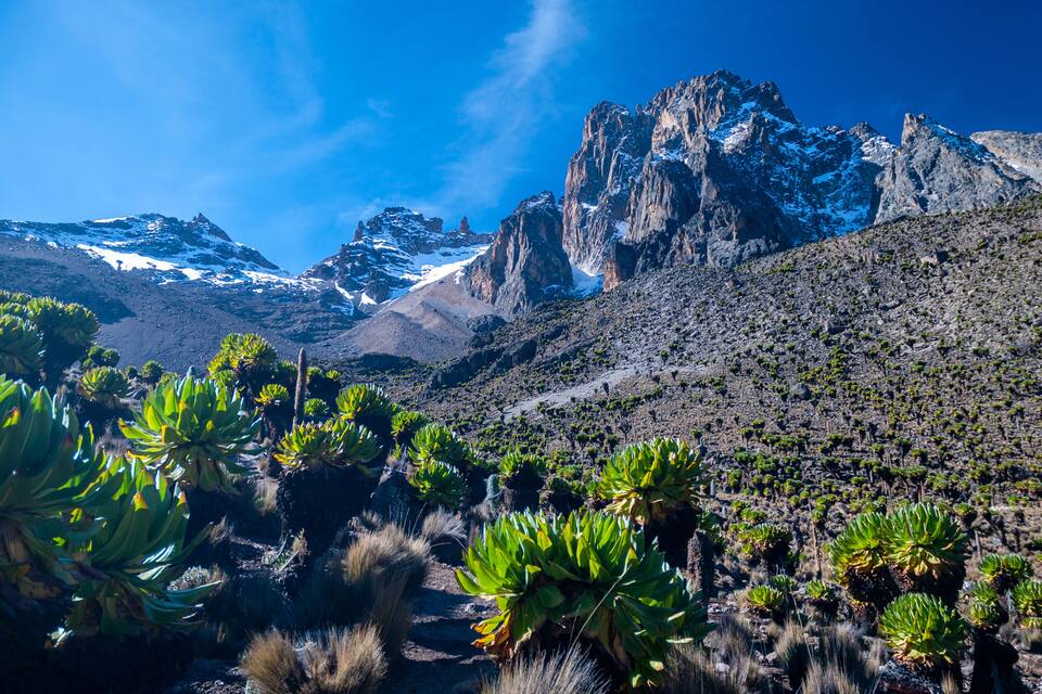 A mountainous landscape with snow-capped peaks, green vegetation, and rocky terrain.