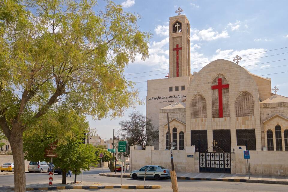 A church with a prominent red cross, a tall tower, and a stone facade.
