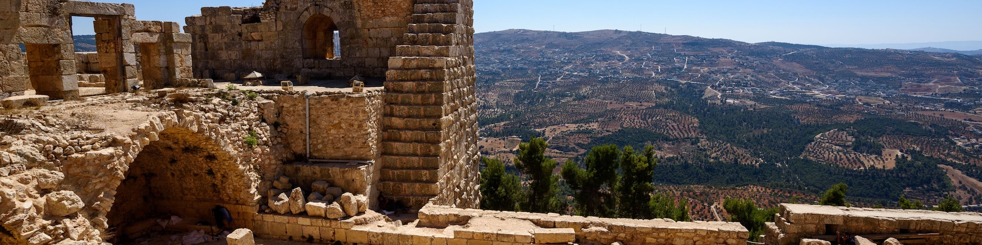 Ancient ruins with stone walls and arches, set against a backdrop of a mountainous landscape.
