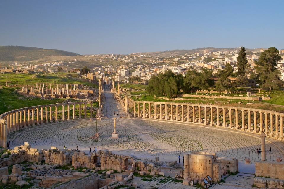 An ancient amphitheater with ruins and columns, surrounded by a cityscape and greenery.