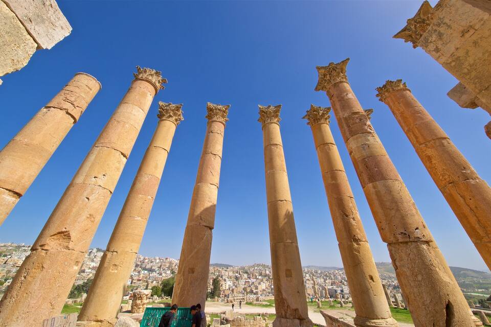 Ancient stone columns with capitals, set against a clear blue sky, overlooking a cityscape.