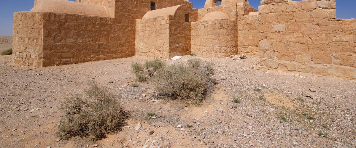 An ancient stone structure with arches and domes in a desert landscape.