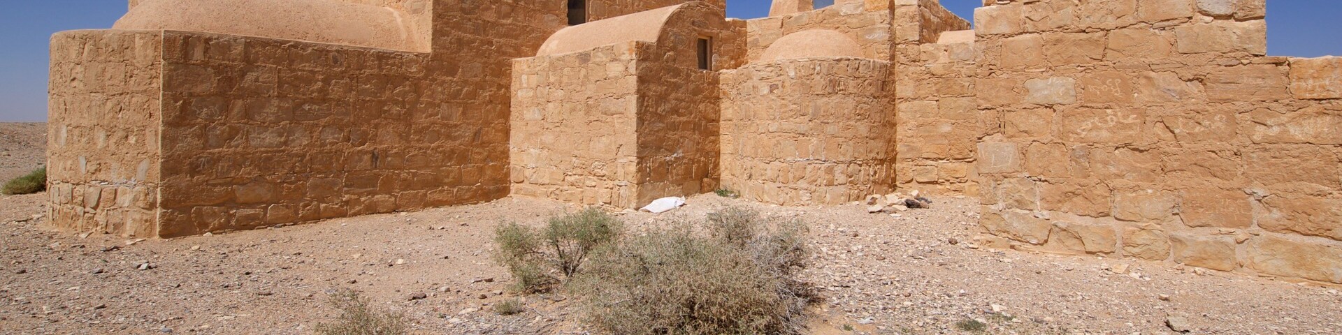 An ancient stone structure with arches and domes in a desert landscape.
