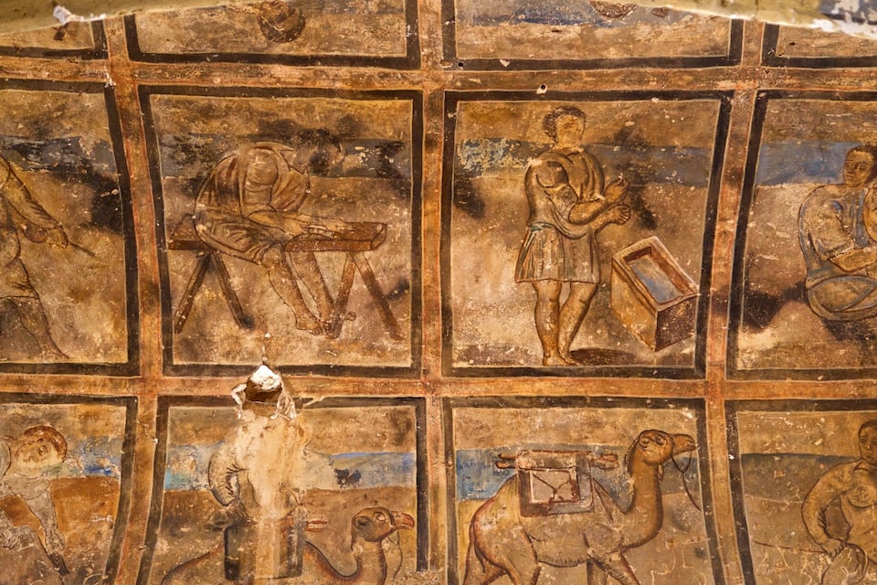 A mosaic with geometric patterns and figures, including a seated figure with a staff and a standing figure with a box.