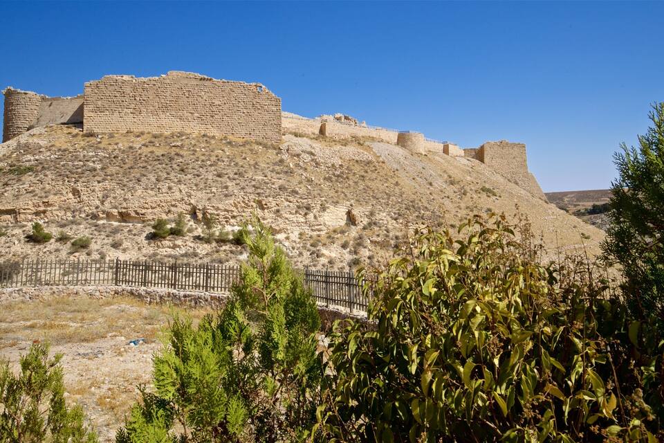 A historical stone fortress on a hill with sparse vegetation.