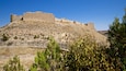 Una fortaleza de piedra histórica en una colina con vegetación escasa.