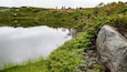A calm lake surrounded by lush greenery and a rocky outcrop.