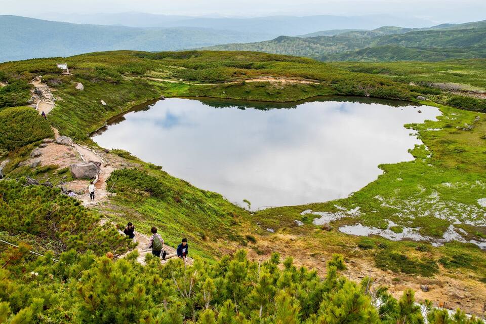 A heart-shaped lake surrounded by green hills and a hiking trail.