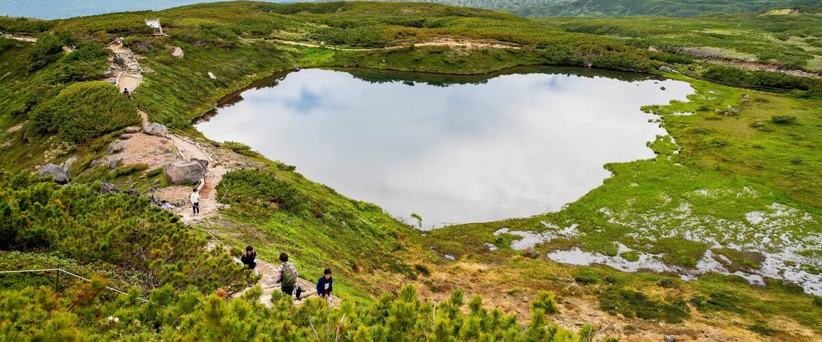 A heart-shaped lake surrounded by green hills and a hiking trail.