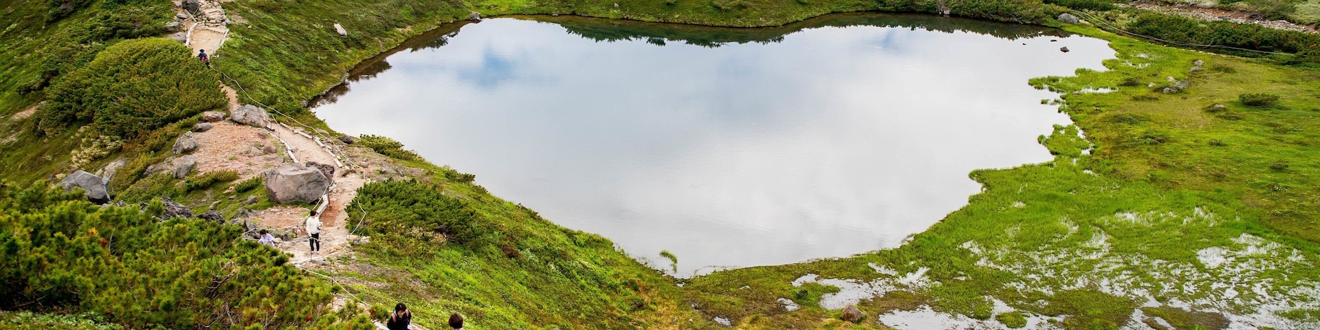 A heart-shaped lake surrounded by green hills and a hiking trail.