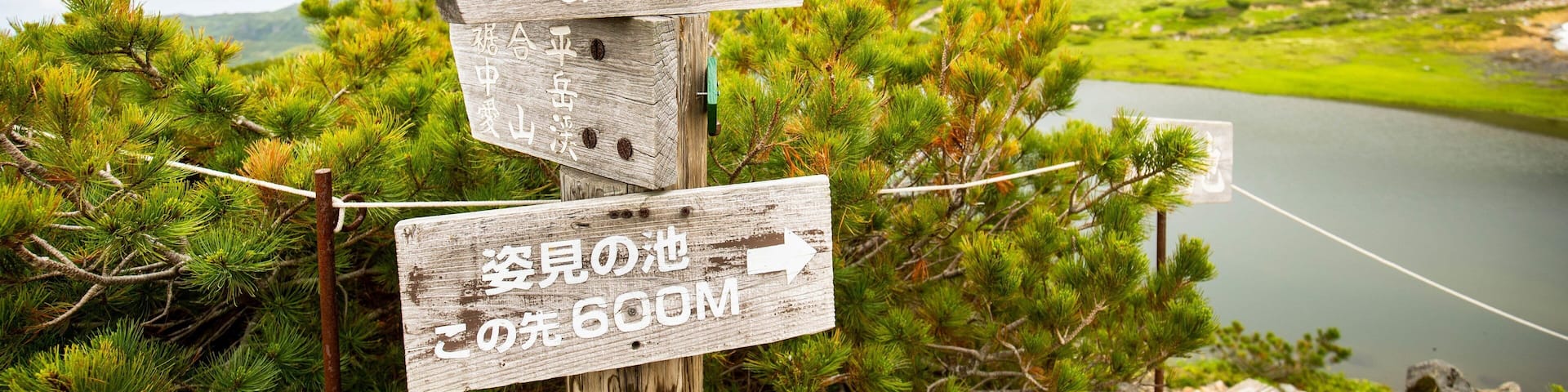 Un cartel de madera con múltiples indicaciones de dirección en una zona montañosa con un lago al fondo.