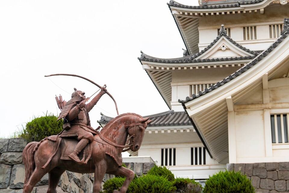 Una estàtua de bronze d'un guerrer a cavall davant d'un edifici tradicional japonès.